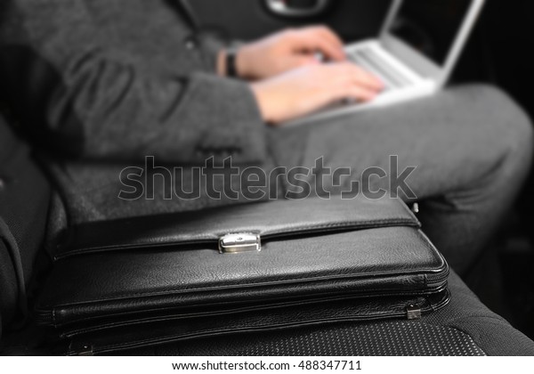 Black leather briefcase and businessman with laptop\
in car