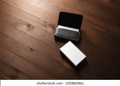 Black leather card holder with blank white business cards on wood table background.