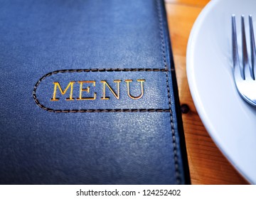 Black Leather Menu With White Plate On Wood Table.