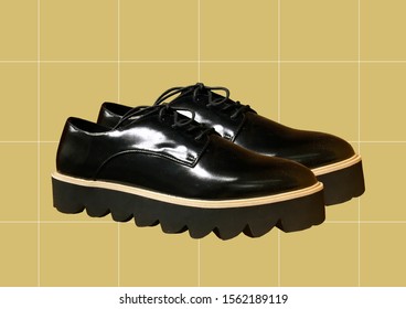 Black Leather Platform Shoes Isolated On Yellow Background. Classic Shoes On A High Black Tractor Platform. Fashionable Strict Low-heeled Shoes. Women Loafers With Lacing. Composition Of Clothes