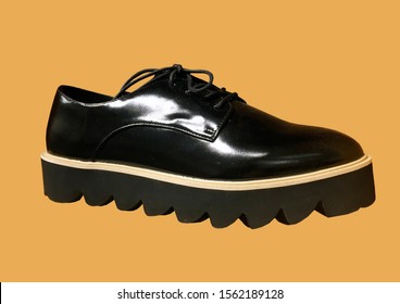 Black Leather Platform Shoes Isolated On Yellow Background. Classic Shoes On A High Black Tractor Platform. Fashionable Strict Low-heeled Shoes. Women Loafers With Lacing. Composition Of Clothes