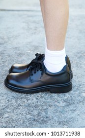 Black Leather School Shoes Worn By A Girl Student, View Of Legs With White Socks On Cement Path