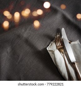 Black Linen Tablecloth With Fine Silver Cutlery And Golden Bokeh For A Romantic Dinner