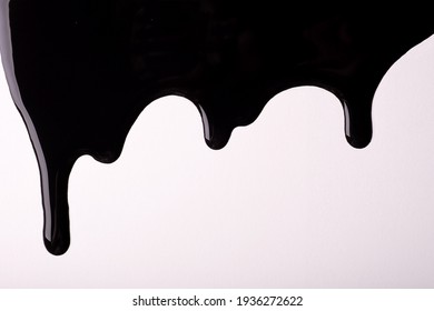 Black liquid drops of paint color flow down on isolated white background. Abstract dark backdrop with fluid drip pattern. Acrylic painting with copy space.