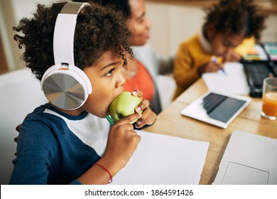 Black Little Boy With Headphones Having An Apple For A Snack While Homeschooling. 