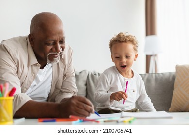Black Little Boy And His Grandfather Sketching Drawing A Picture Together Using Colorful Markers Sitting At Desk At Home. Grandpa And Grandson Having Fun Spending Time On Weekend Indoor