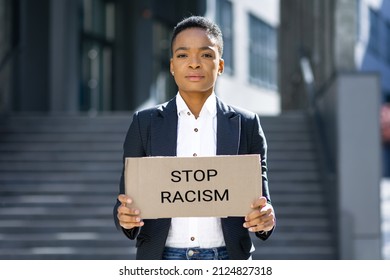 Black Lives Matter. A Serious Black African Woman Protesting In Front Of A Poster Community Against The Lawlessness Of Black Citizens Stands On The Street