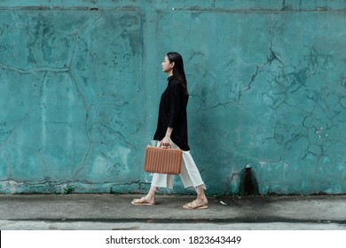 Black long hair woman in black shirt walking alone along the old green wall with wooden basket.
