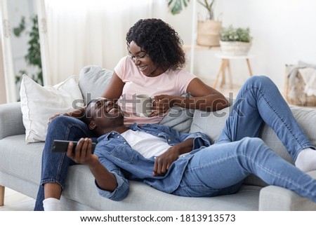 Black lovers spending weekend together at home, watching TV and drinking tea at living room, empty space