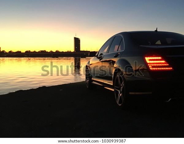 川の横に停めた黒い高級セダン車で 光が灯り 夕日が水に映る の写真素材 今すぐ編集
