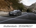 Black luxury sedan cruising along a winding mountain road, surrounded by rugged hills and pine trees, showcasing a dynamic drive and scenic beauty.