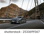 Black luxury sedan driving across a modern suspension bridge with a rugged mountain backdrop, capturing a sense of speed and adventure.