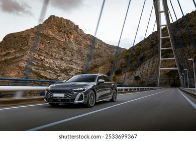 Black luxury sedan driving across a modern suspension bridge with a rugged mountain backdrop, capturing a sense of speed and adventure. - Powered by Shutterstock