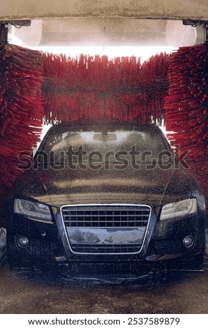 The black machine is on an automatic car wash and is vigorously washed by three red brushes from all sides