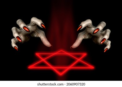 Black magic ritual. Scary witches hands with red long nails and a burning hexagram symbol in the dark, low key, selected focus.