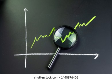Black magnifying glass on chalk drawing green line stock or company performance graph and chart on blackboard using as financial analysis, profit and loss or searching for earning and yield.