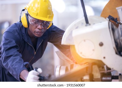 Black male african american workers wear sound proof headphones and yellow helmet working an iron cutting machine in background factory Industrial. - Shutterstock ID 1931560007