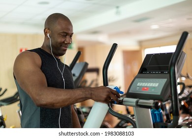 Black Male Athlete Cleaning A Cardio Machine With Disinfectant At The Gym. Selective Focus.