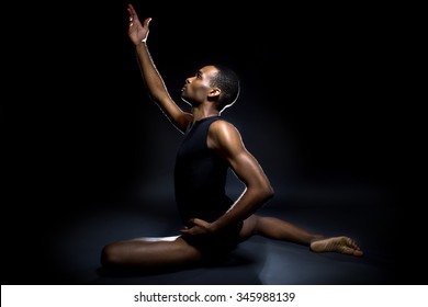 Black male dancer practicing warm up exercises for flexibility.  He is lit for contrast to outline the human body.  - Powered by Shutterstock