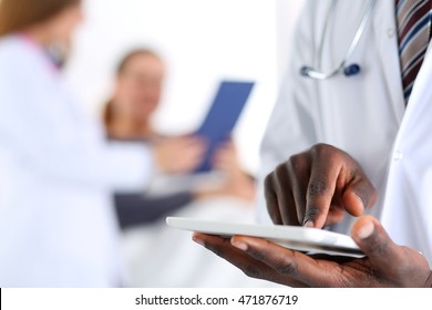 Black Male Doctor Hand Point With Finger In Digital Tablet Pc Touch Screen With Patient Lying In Bad In Background. Professional Equipment, Therapeutist Ward Round, Search Opportunities Concept