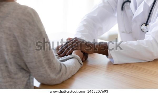 Black male doctor holding hands of female patient at\
meeting as women health medical care concept express trust support\
empathy about miscarriage, help hope in cancer disease therapy,\
close up view