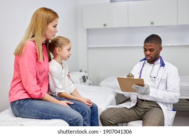 Black Male Doctor Listen Consult Girl Make Notes In Patient Card At Medical Checkup Appointment, Awesome Child With Mom Visit Pediatrician Talk In Clinic, Children Healthcare Concept