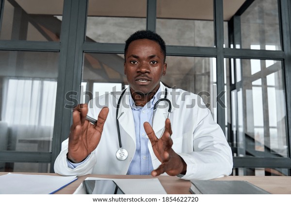 Black male doctor talking to web cam consulting\
patient via virtual telemedicine advice. African physician making\
online telehealth video call for remote appointment tele health\
care chat. Webcam view