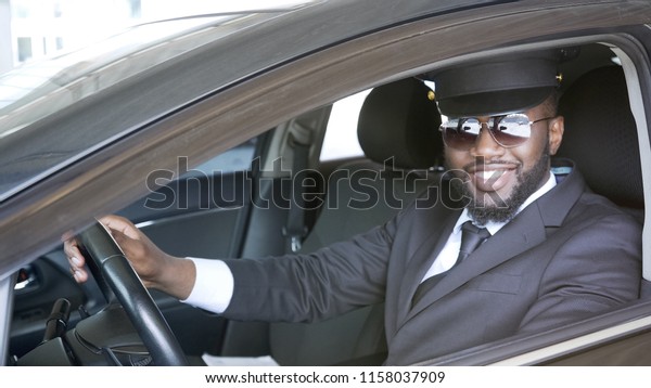 Black male driver sitting in car and smiling into\
camera, transportation\
service