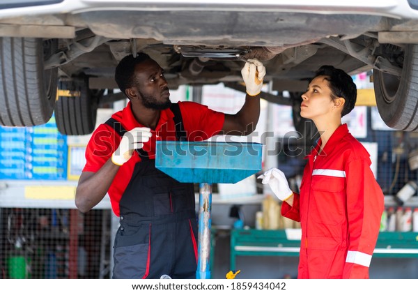 Black Male And\
Female trainee Mechanics Working Underneath Car Together Car\
maintenance and auto service garage.\
