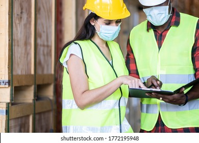 Black Male And Female Workers Talking In Warehouse Store. Woman And Man Engineers People Wear Safety Hard Helmet, Vest And Face Mask Checking Storage Box Parcel In Factory During Covid 19 Pandemic.