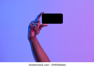 Black Male Hand Holding Blank Smartphone In Horizontal Orientation Over Purple Neon Background, African American Man Demonstrating Copy Space For App Or Mobile Game Design, Mockup Image