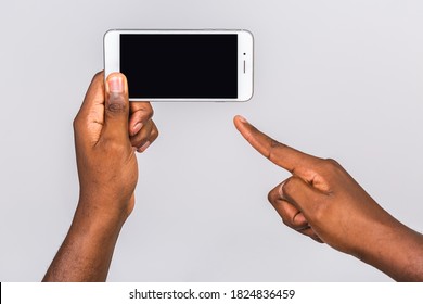 Black male hand touching mobile phone display and pointing with index finger at blank screen, isolated over white background, copy space, cutout.