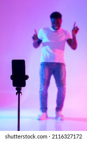 Black male influencer shooting video for social media on mobile phone, having fun in neon light, mockup. African American blogger live streaming content for vlog, broadcasting online, selective focus