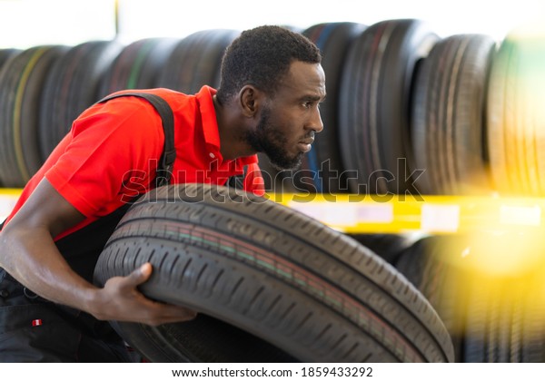 Black male Mechanic holding a\
tire and showing wheel tires at car repair service and auto store\
shop. Expertise mechanic working in automobile repair garage.\
