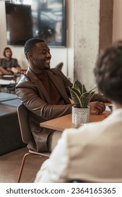 Black male person having fun conversation and smiling during meeting at table with his colleagues - Shutterstock ID 2364165365