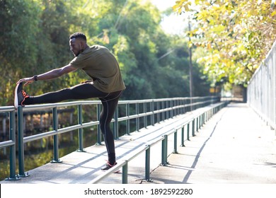 Black Male Runner Doing Stretching Exercise Beside Road In Park At Autumn Morning. 