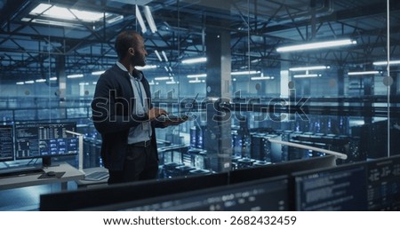 Black Male Software Developer Analyze System Performance Metrics on a Laptop Inside a Modern Data Center. Young Manager Ensuring Efficient Operations for Critical Infrastructure