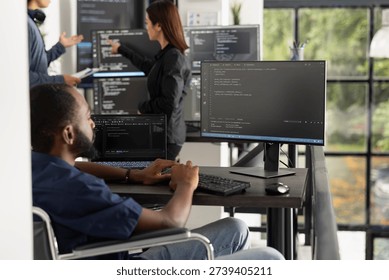 Black male software developer sits at office workstation, focused on computer coding tasks. Motivated professional in tech industry highlights disability inclusion, ambition and digital productivity.