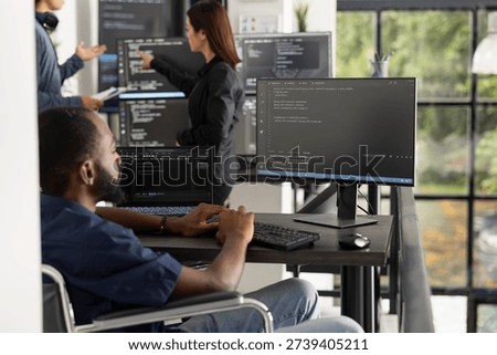 Black male software developer sits at office workstation, focused on computer coding tasks. Motivated professional in tech industry highlights disability inclusion, ambition and digital productivity.