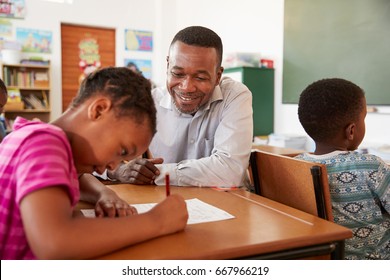 Black Male Teacher Helping Elementary School Girl In Class