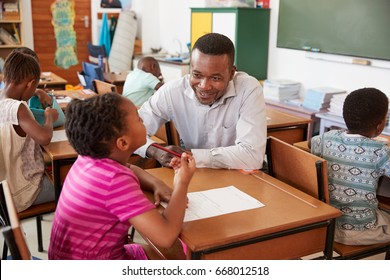 Black Male Teacher Helping Elementary School Girl In Class