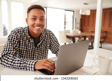 Black Male Teenager Using A Laptop Computer At Home Smiling To Camera, Close Up