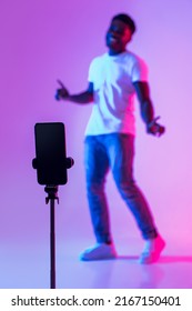 Black male vlogger shooting video for social media on cellphone, having fun in neon light, mockup. African American influencer live streaming content for his blog, broadcasting online, selective focus
