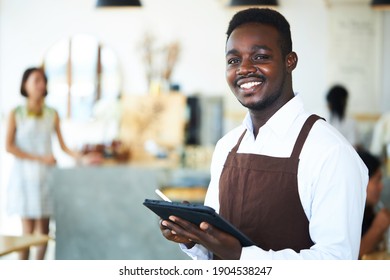 A black male waiter is standing and holding the tablet and friendly smiling for the wait to welcome customers in the restaurant.