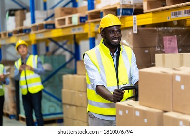 Black Male Warehouse Worker Pulling A Pallet Truck. Middle Aged African American Warehouse Worker Preparing A Shipment In Large Warehouse Distribution Centre