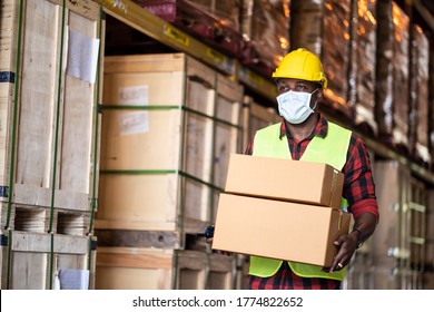 Black male workers wearing protective face mask working in factory warehouse. Black man carrying box parcel walking indoor of building during covid 19 pandemic crisis. Logistic industry concept.