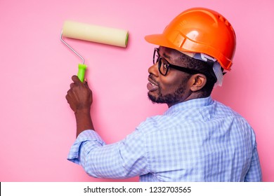 Black Man African American Holding Paint Roller In Hand Paints The Wall In Pink Color .happy African Builder Painting Inside The House,businessman Wears A Helmet Hard Hat.young Guy Is Painting