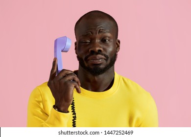 Black man with annoyed face expression talking on phone on pink background. Portrait of african american male model with unhappy "whatever" face expression with purple landline phone 