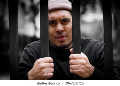 Black Man Behind Bars And In Jail. Hands Clasped Against Metal Bars