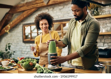 Black man blending healthy food while preparing smoothie with is wife in the kitchen.
